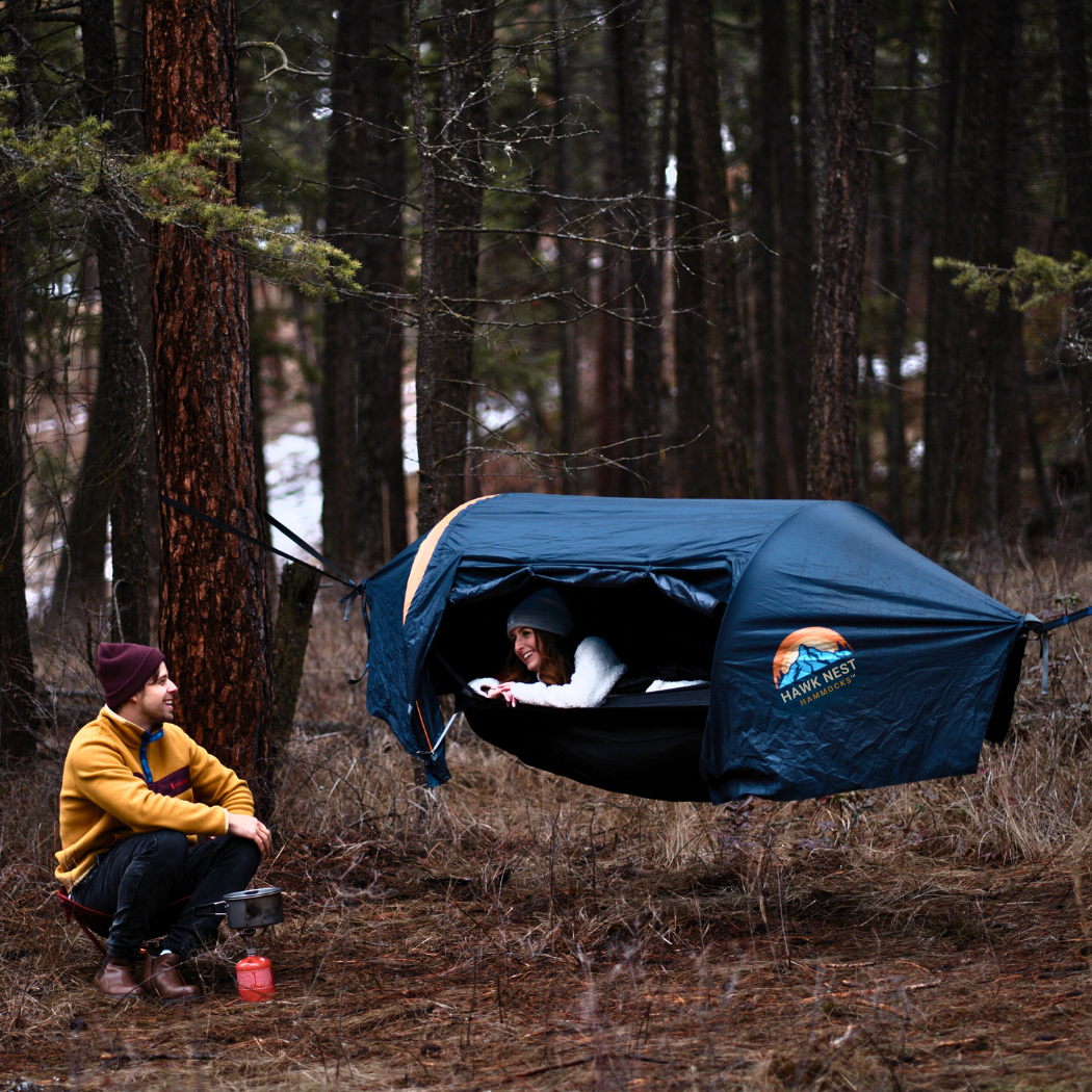 Ultralight hammock tent suspended between trees, ideal for outdoor camping and backpacking adventures. Compact, lightweight design ensures easy portability and setup. Perfect shelter solution for nature lovers seeking comfort and convenience in the wilderness. Two campers look at echother