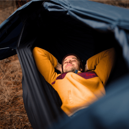 Ultralight hammock tent suspended between trees, ideal for outdoor camping and backpacking adventures. Compact, lightweight design ensures easy portability and setup. Perfect shelter solution for nature lovers seeking comfort and convenience in the wilderness. A camper is shown resting in the hammock